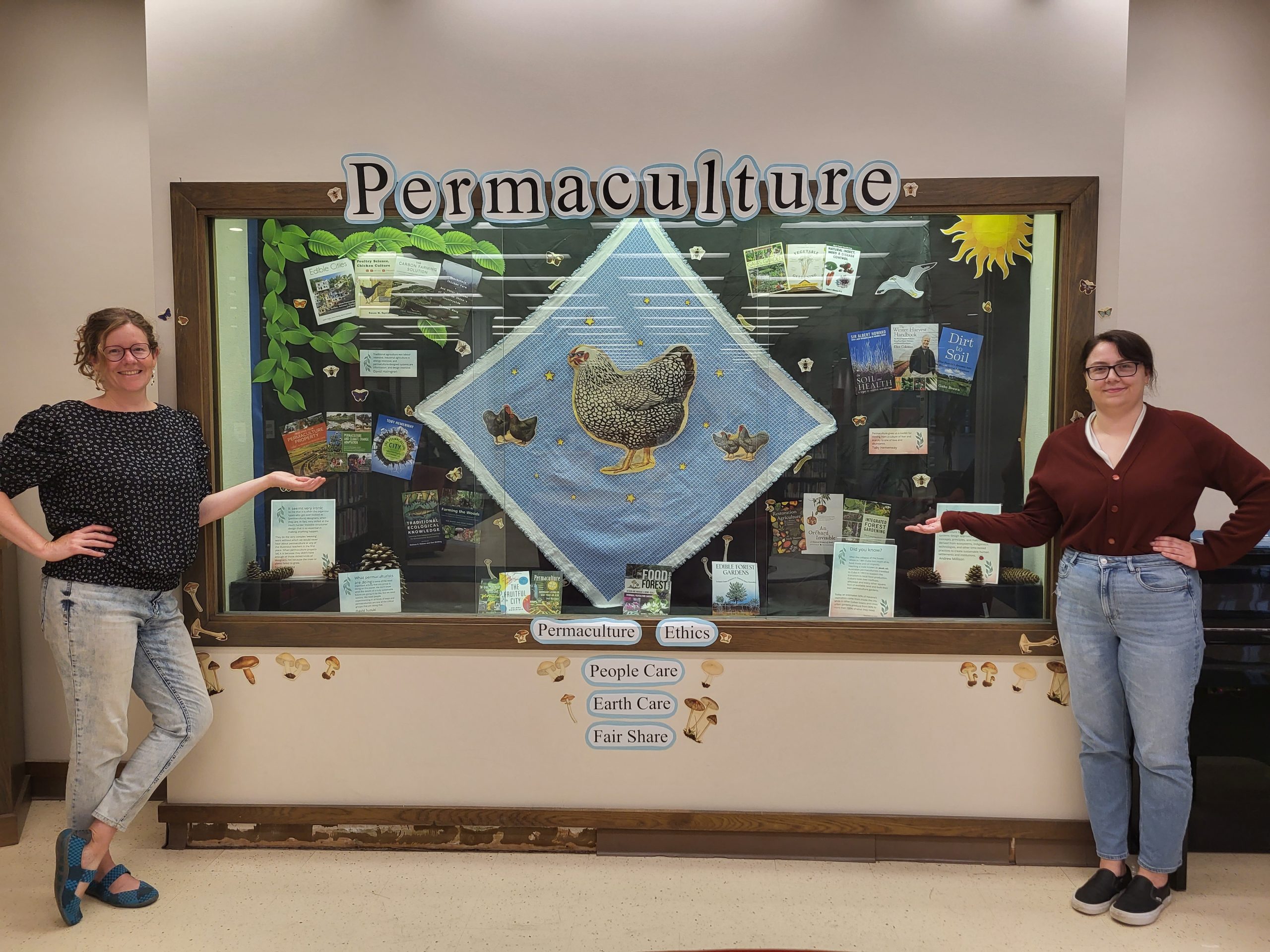 Image of display case with permaculture exhibit featuring its two creators, Elizabeth and Jessica